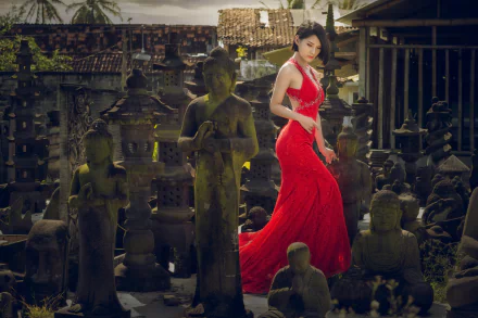 A brunette woman in a flowing red dress poses amidst a serene collection of Buddha statues, creating a striking contrast in this HD desktop wallpaper.