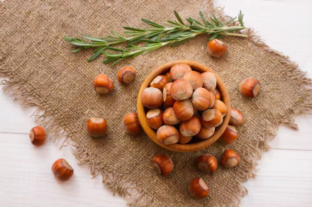 A rustic bowl filled with hazelnuts sits on a textured burlap background, accompanied by fresh rosemary, showcasing food in stunning 8K Ultra HD detail.