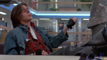 HD desktop wallpaper featuring Judd Nelson as John Bender from the movie The Breakfast Club, sitting confidently in a school library setting.