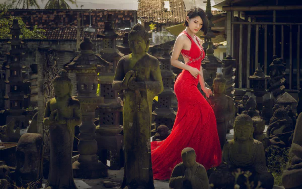 A brunette woman in a flowing red dress poses amidst a serene collection of Buddha statues, creating a striking contrast in this HD desktop wallpaper.