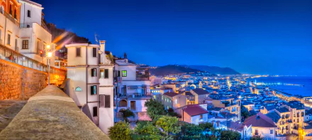 Night view of a man-made town in Amalfi, Italy, featuring houses along the horizon under a deep blue sky in stunning 4K Ultra HD quality.