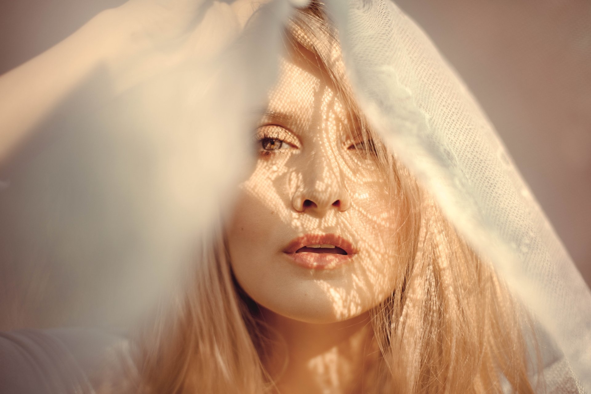 Close-up of a blonde woman’s face softly lit by sunshine, partially obscured by a delicate veil, captured in stunning 8K Ultra HD quality.