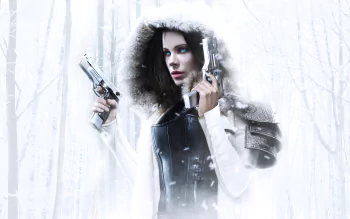 HD wallpaper featuring Kate Beckinsale as Selene in Underworld: Blood Wars, showcasing her armored outfit and holding guns in a snowy, forested background.