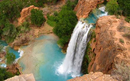 HD PC desktop wallpaper: aerial view of Havasu Falls — turquoise pool and white cascade over red rock cliffs, surrounded by green trees; vivid nature waterfall background.