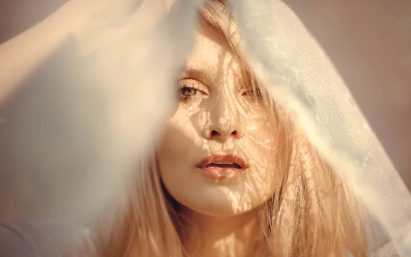 Close-up of a blonde woman’s face softly lit by sunshine, partially obscured by a delicate veil, captured in stunning 8K Ultra HD quality.