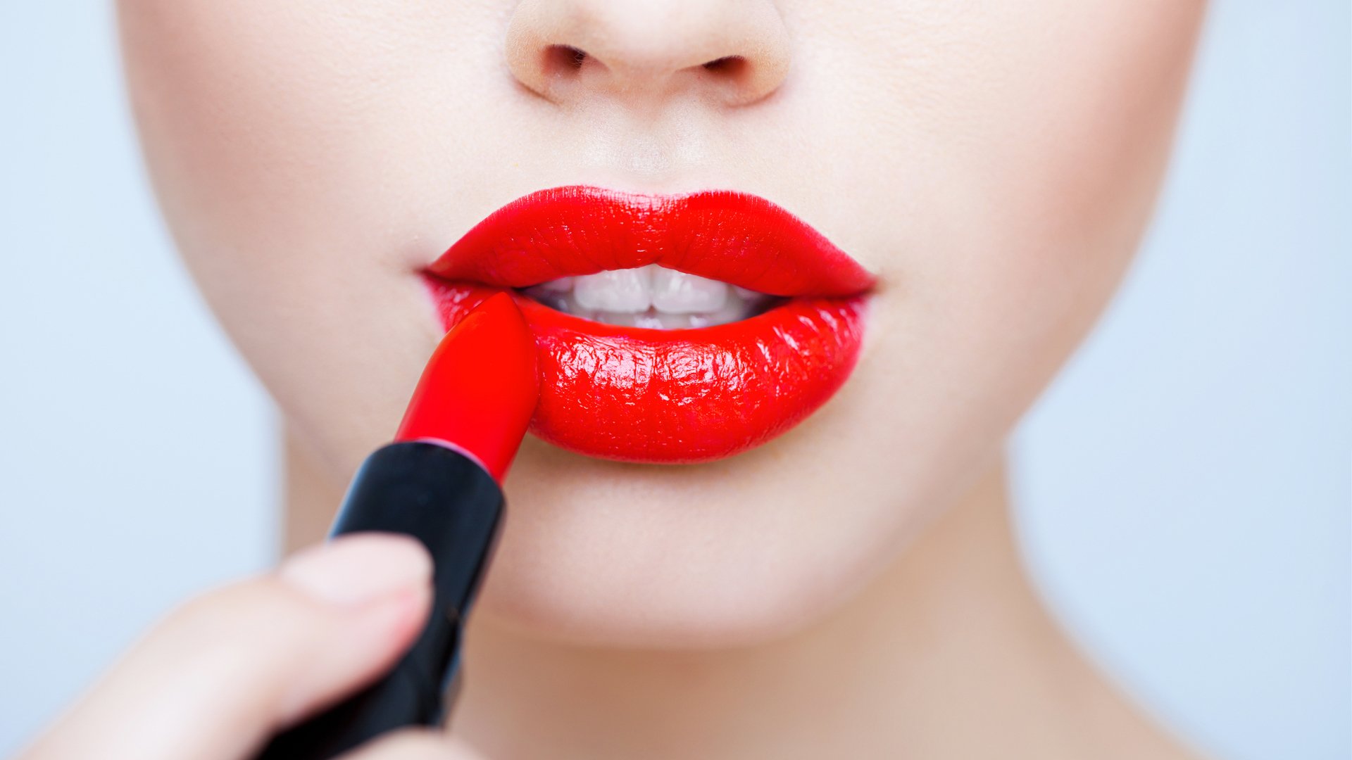 Close-up HD desktop wallpaper of a woman applying vibrant red lipstick to her lips, highlighting smooth skin and glossy texture.