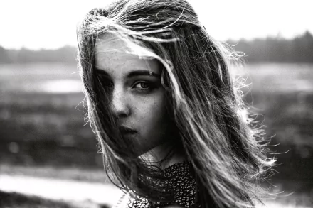 Black and white HD desktop wallpaper of a woman’s face in sunlight, with wind-swept hair and a blurred natural background.