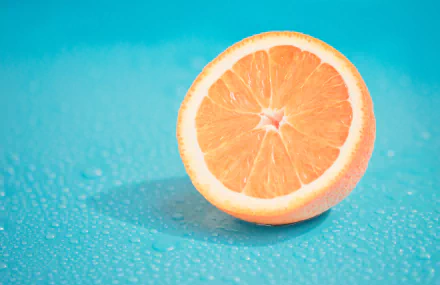HD desktop wallpaper featuring a close-up of a fresh orange fruit half against a vibrant blue background, highlighting the bright orange color and juicy texture.