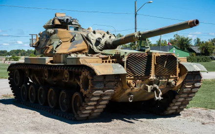 HD PC desktop wallpaper showing an M60 Patton military tank in desert camouflage parked outdoors under a clear blue sky.
