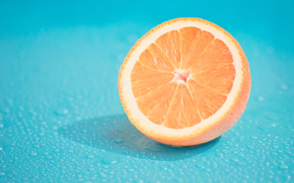 HD desktop wallpaper featuring a close-up of a fresh orange fruit half against a vibrant blue background, highlighting the bright orange color and juicy texture.