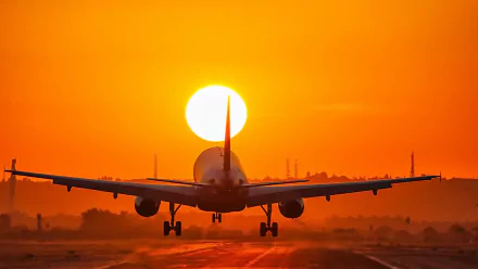 A passenger plane takes off against a vibrant orange sunset, casting a warm glow over the horizon. This HD image captures a stunning moment in aviation.