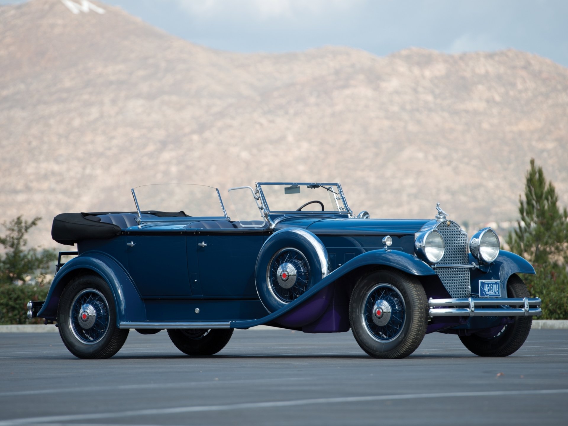 HD desktop wallpaper of a blue 1931 Packard Deluxe Eight Sport Phaeton convertible parked with desert mountains in the background.