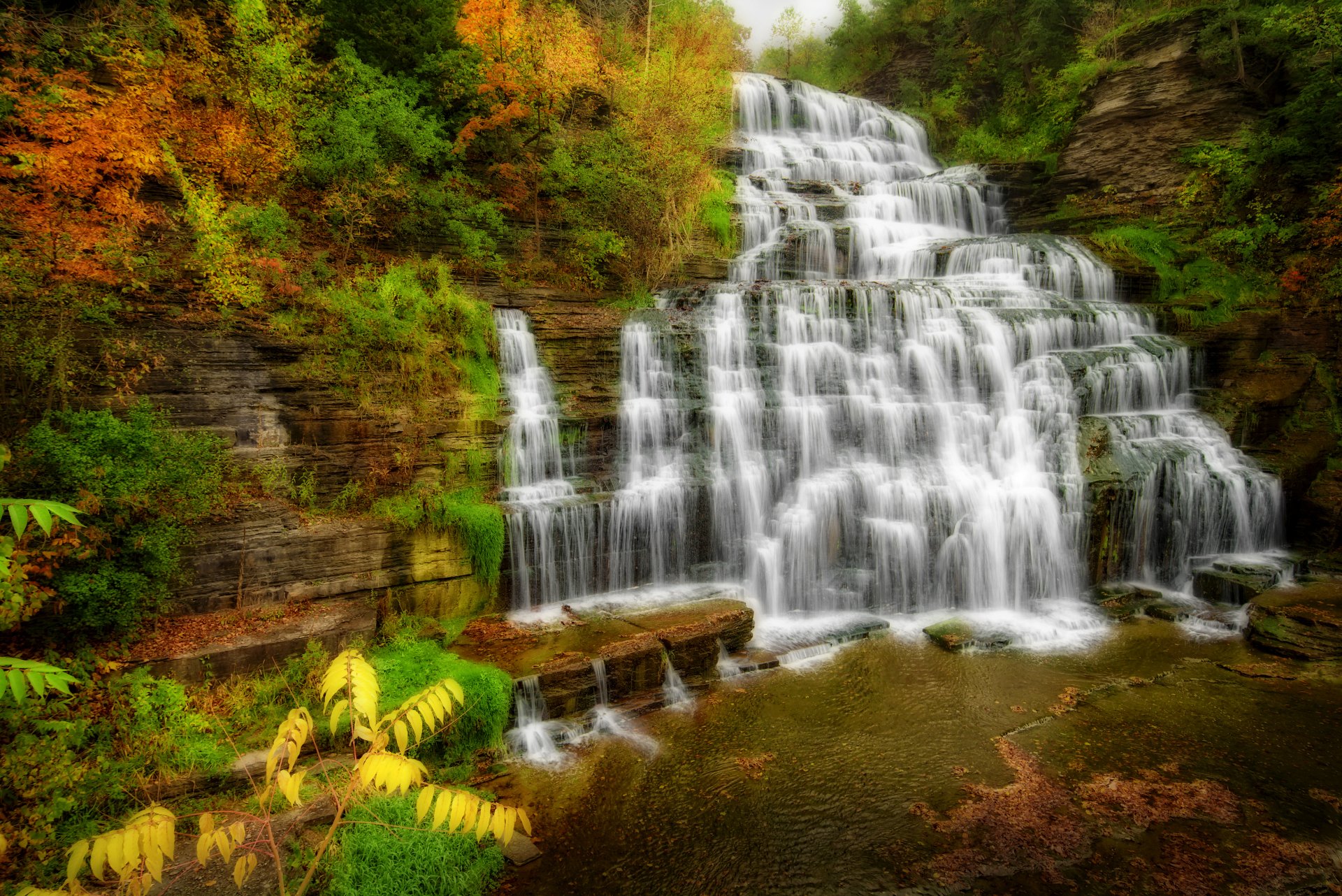 HDR 4K Ultra HD PC desktop wallpaper: fall nature scene of a tiered waterfall cascading over rock ledges amid vivid autumn foliage.