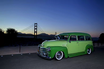 HD PC desktop wallpaper featuring a green lowrider 1952 Chevrolet Suburban parked by a bridge at dusk.