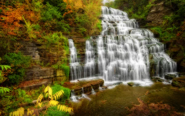 HDR 4K Ultra HD PC desktop wallpaper: fall nature scene of a tiered waterfall cascading over rock ledges amid vivid autumn foliage.