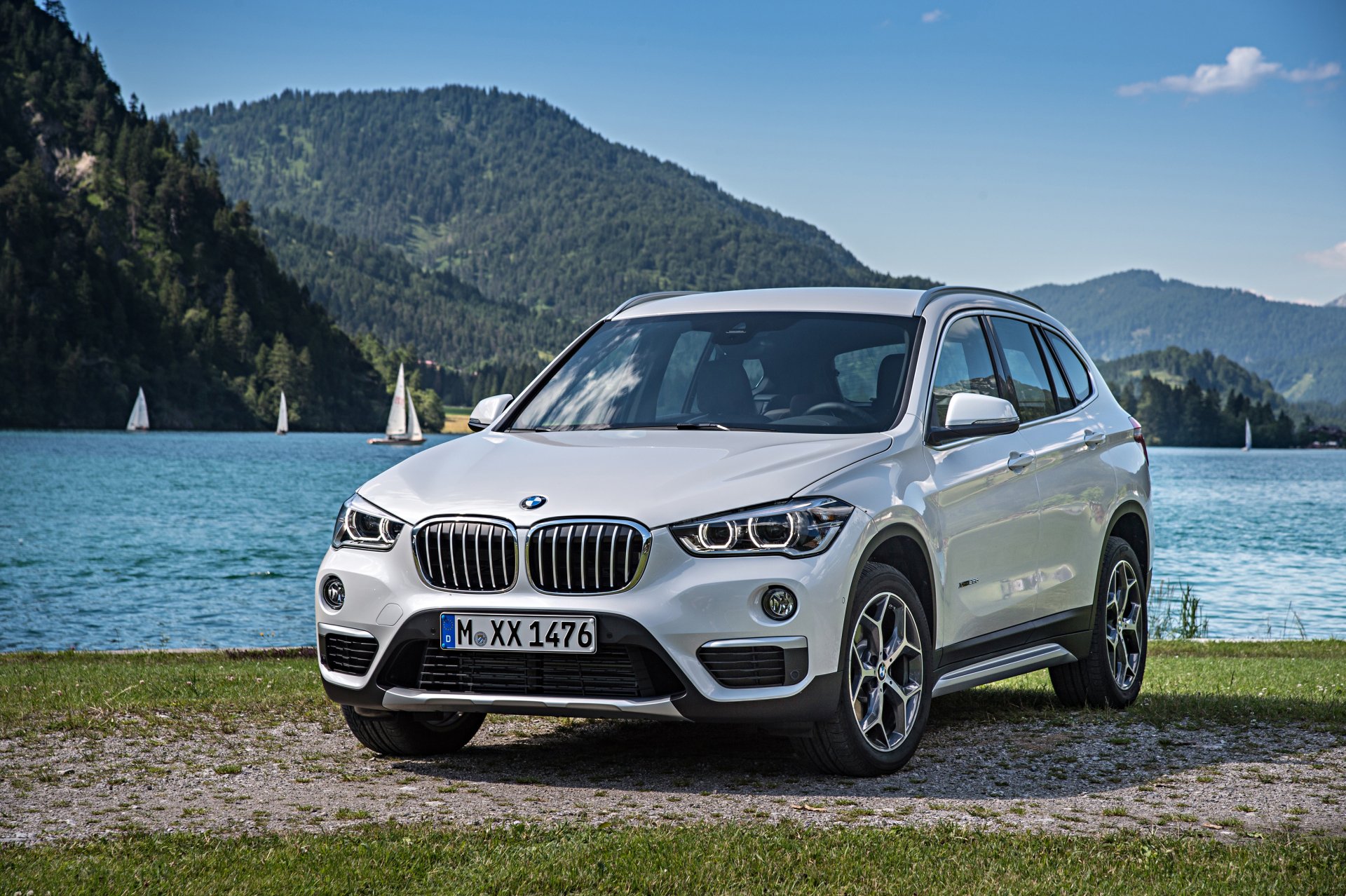 White BMW X1 SUV parked by a lake with forested mountains and blue sky — 4K Ultra HD PC desktop wallpaper and background.
