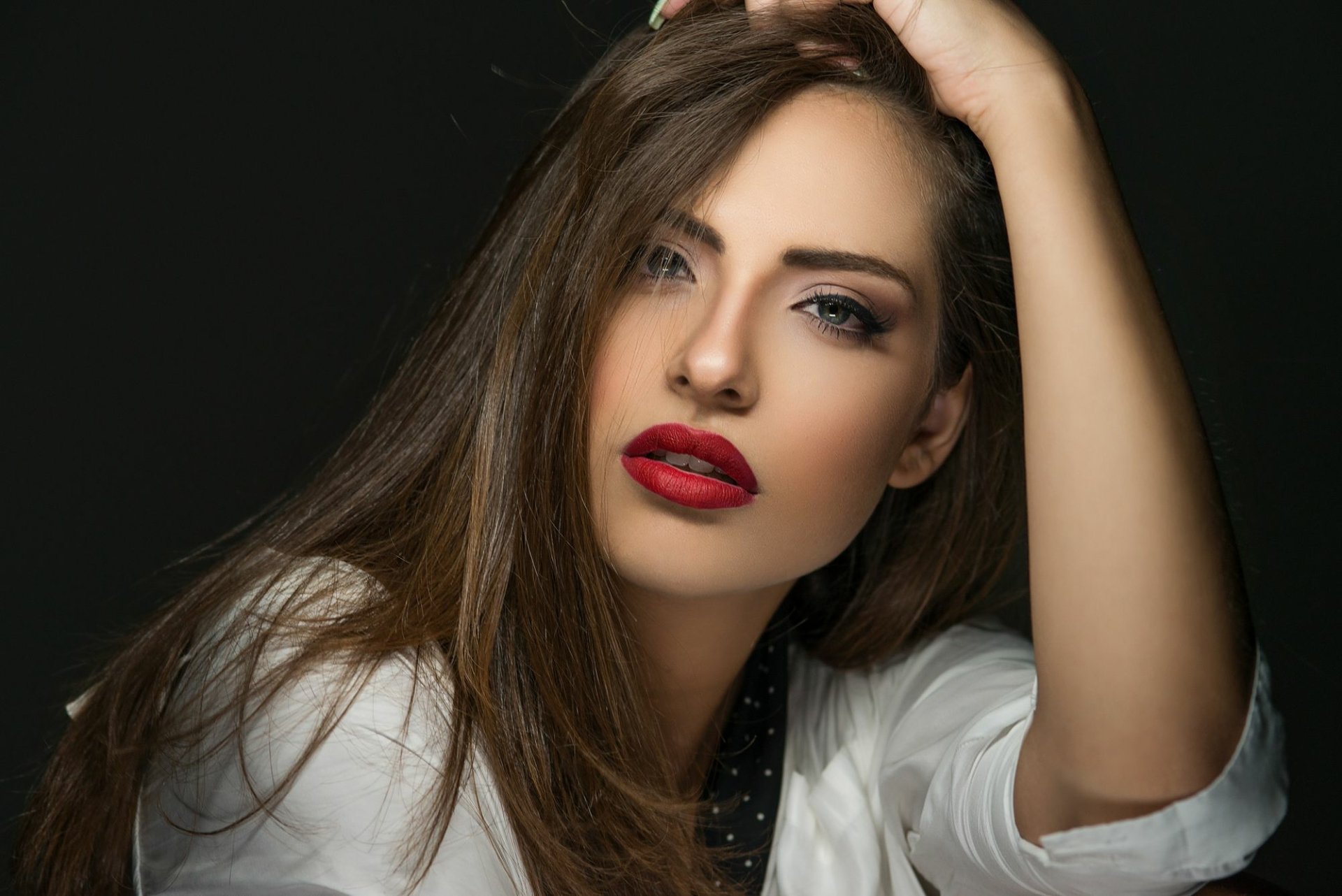 A brunette woman with striking red lipstick poses confidently against a dark background, showcasing her model-like features in this HD desktop wallpaper.