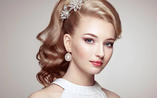 HD desktop wallpaper featuring a blonde woman with blue eyes and elegant earrings, showcasing a refined hairstyle with decorative hairpieces. The model's serene expression adds to the image's grace and sophistication.
