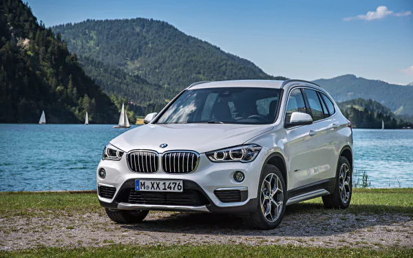 White BMW X1 SUV parked by a lake with forested mountains and blue sky — 4K Ultra HD PC desktop wallpaper and background.