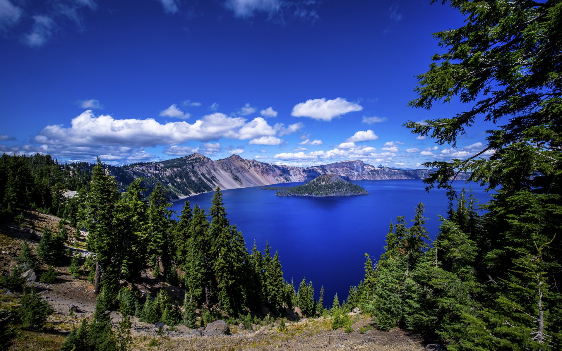 A vibrant 4K Ultra HD view of Crater Lake in Oregon, showcasing deep blue water surrounded by lush green trees and rugged cliffs under a bright sky.