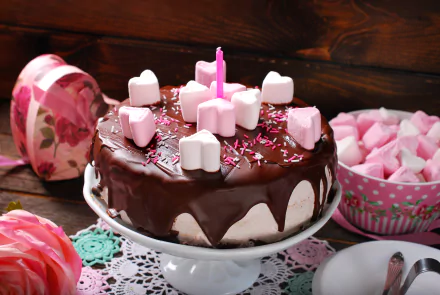 4K Ultra HD image of a chocolate cake topped with heart-shaped marshmallows and a single pink candle, surrounded by a floral box and a bowl of marshmallows on a wooden table.