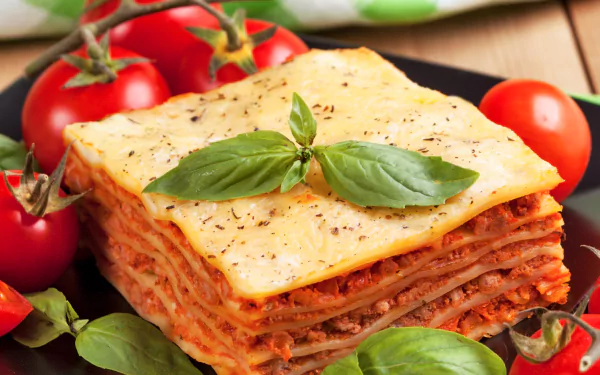 HD desktop wallpaper featuring a close-up of a layered lasagna topped with fresh basil, surrounded by ripe tomatoes, highlighting rich colors and textures of the food.