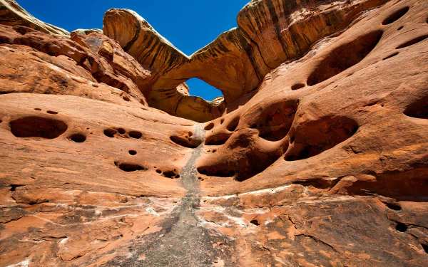 HD desktop wallpaper of red sandstone rock formations and erosional holes beneath a natural arch in Canyonlands National Park, Utah, USA, set against a vivid blue sky.