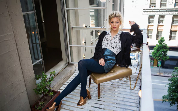 HD desktop wallpaper featuring American actress and singer Olivia Holt, a blonde celebrity, seated stylishly on a balcony in an urban setting.