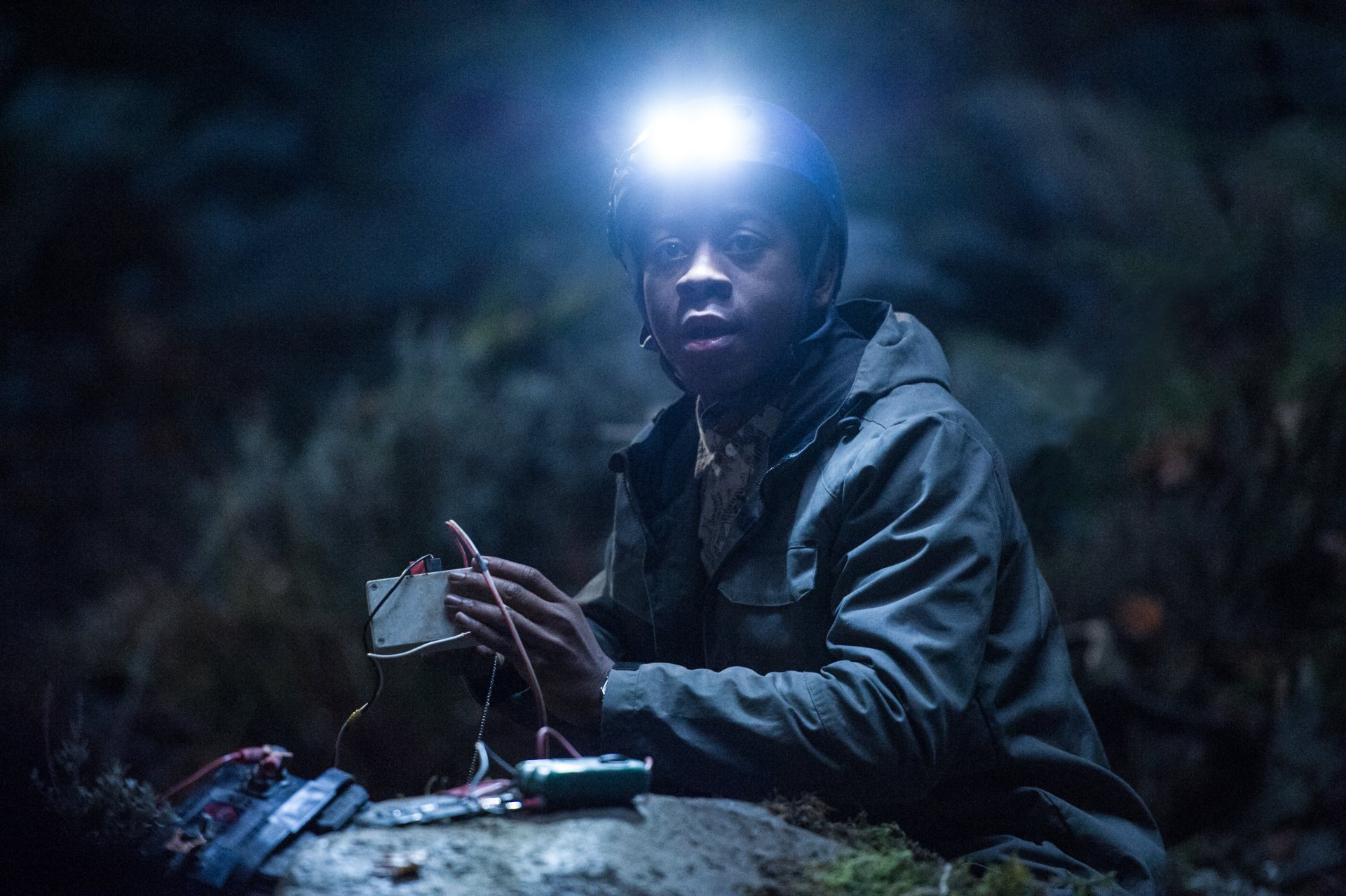 RJ Cyler as Billy Cranston in a scene from the 2017 Power Rangers movie, set in a dark environment with a headlamp illuminating his focused expression. 4K Ultra HD wallpaper.