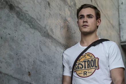 Dacre Montgomery as Jason Lee Scott from the 2017 movie Power Rangers, posed thoughtfully against a concrete wall, wearing a casual white shirt with a graphic design.