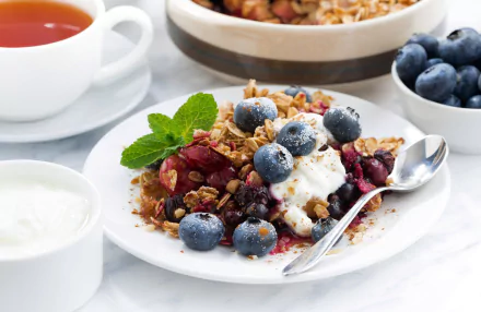 HD desktop wallpaper featuring a fresh breakfast with blueberry-topped muesli, yogurt, and a cup of tea on a white table setting.