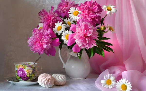A still life featuring vibrant pink peonies and white daisies in a white vase, accompanied by a decorative cup and cookies, set against a soft pink background.