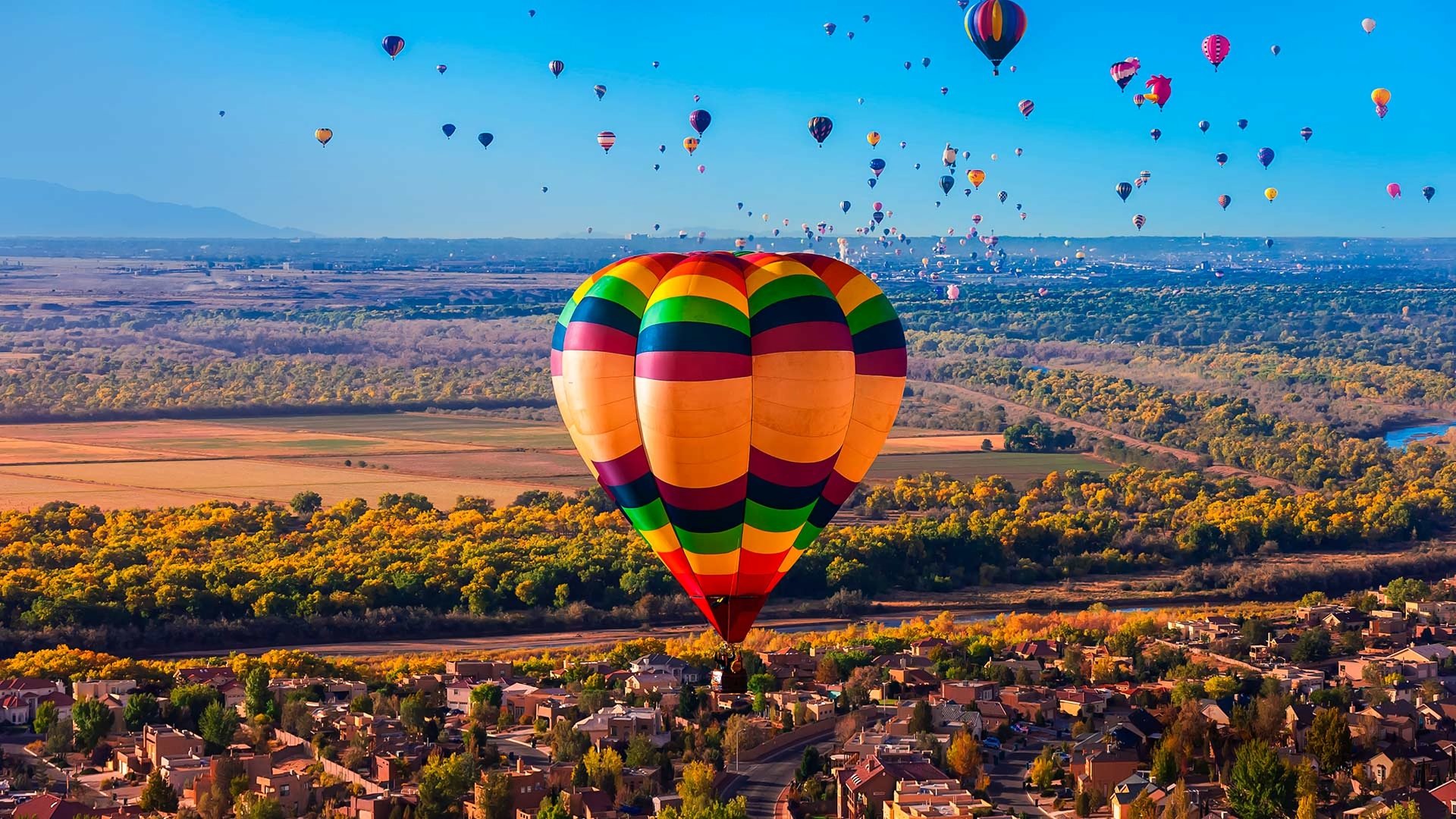 Aerial landscape view of colorful hot air balloons floating over a town near the horizon, captured in a vibrant HD PC desktop wallpaper.