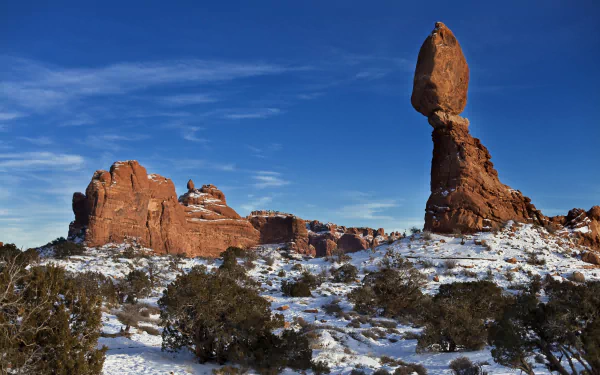 Winter landscape of snow-dusted sandstone formations in Arches National Park, Utah, USA, showcasing the desert's natural beauty under a clear blue sky.