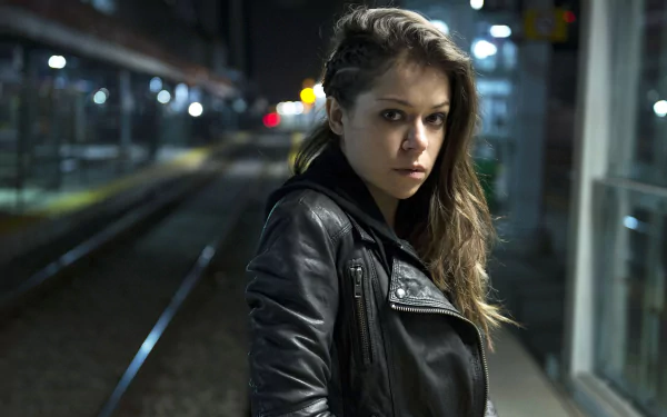 Tatiana Maslany, Canadian actress with brown eyes and brunette hair, stands confidently on a dimly lit train platform in this HD desktop wallpaper.
