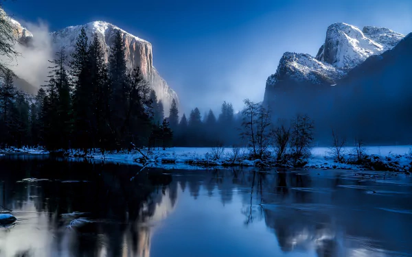 HD desktop wallpaper of Yosemite National Park on a winter night, showing snow-covered mountains, trees, fog, and their reflections in a calm lake.