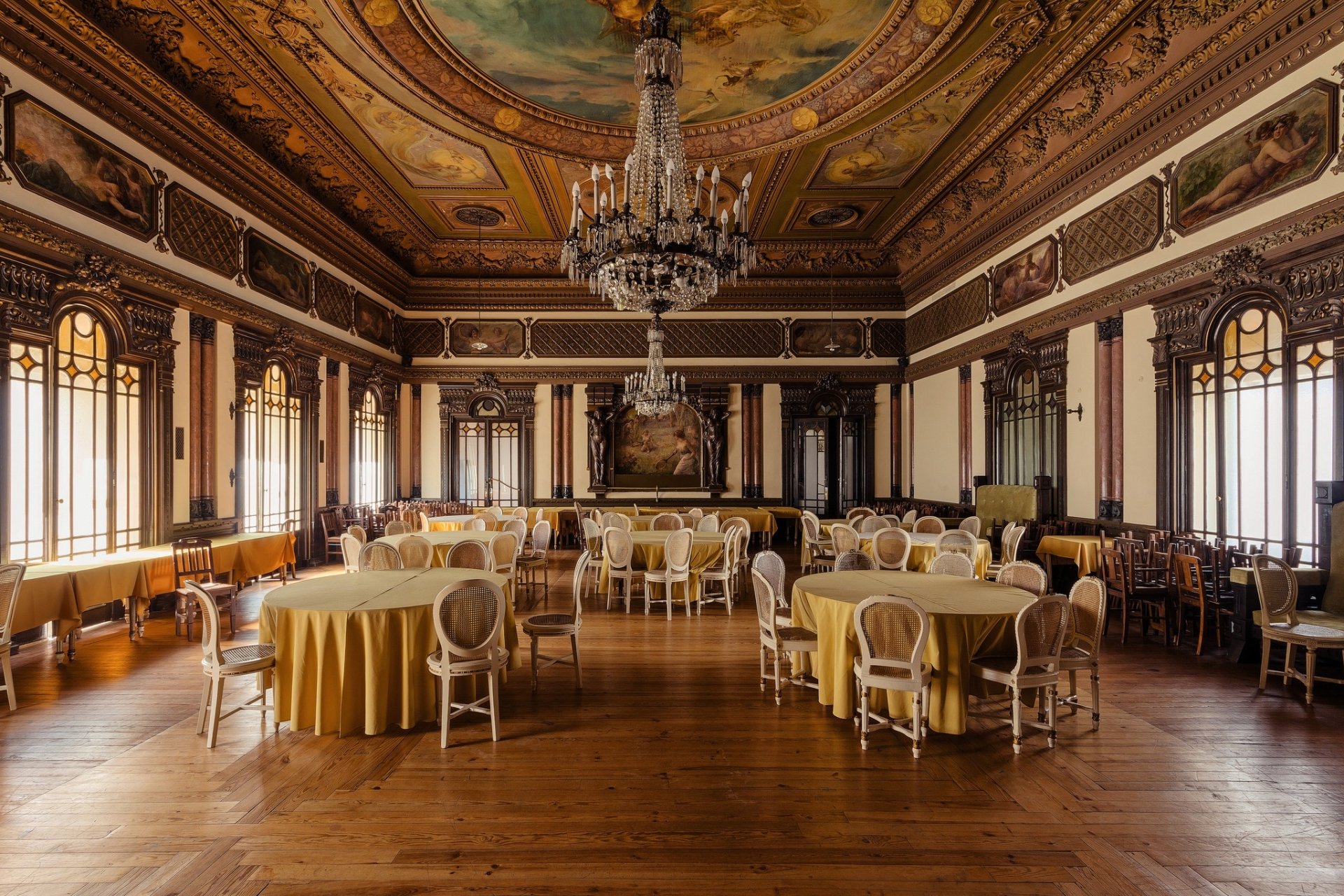 HD desktop wallpaper of an elegant room with ornate furniture, round tables covered in yellow cloth, large chandelier, and intricate ceiling artwork.