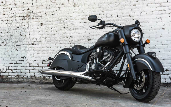 Matte-black Indian Chief Dark Horse motorcycle parked against a weathered white brick wall — HD PC desktop wallpaper and background.