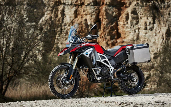 HD desktop wallpaper featuring a BMW F800GS Adventure motorcycle parked on a rugged terrain with rocky cliffs in the background.
