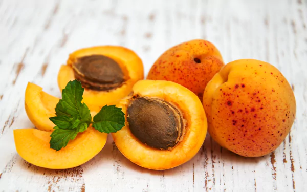 Close-up of ripe sliced peaches and whole fruit with mint on distressed white wood, vivid orange tones — 2K Quad HD PC desktop wallpaper/background