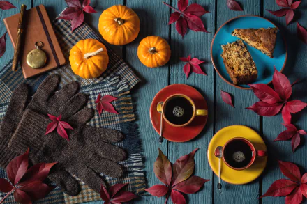 HD still life desktop wallpaper featuring fall pumpkins, red leaves, cozy gloves, coffee in colorful cups, and slices of cake arranged on a rustic blue wooden table.