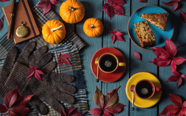 HD still life desktop wallpaper featuring fall pumpkins, red leaves, cozy gloves, coffee in colorful cups, and slices of cake arranged on a rustic blue wooden table.