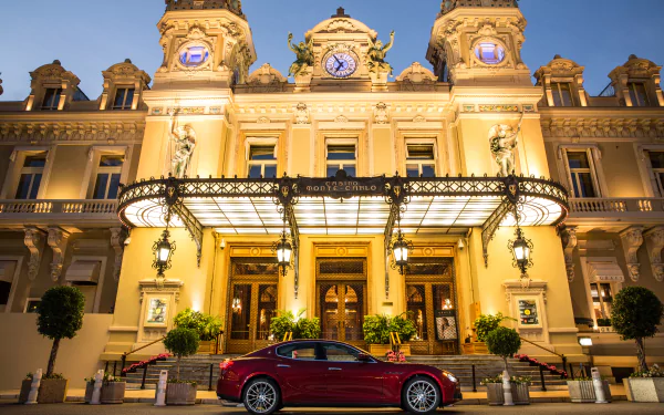 Red Maserati Ghibli parked before a grand illuminated casino at night — 4K Ultra HD PC desktop wallpaper background.