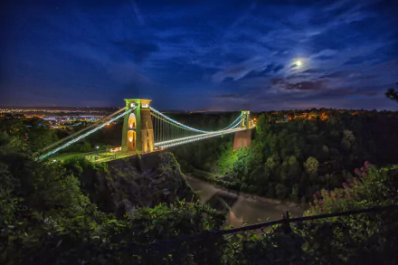 4K Ultra HD desktop wallpaper: Clifton Suspension Bridge in Bristol, England — a man-made span lit at night over tree-lined Avon Gorge, moonlit sky.