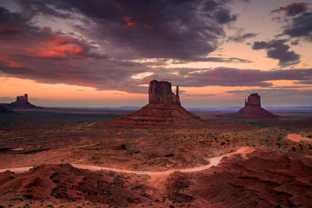 HD desktop wallpaper showing Monument Valley's iconic desert landscape under a dramatic sky with clouds at sunset, capturing the vast horizon in the USA.