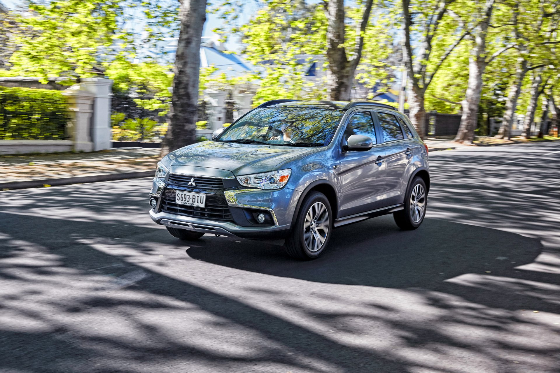Silver Mitsubishi ASX SUV driving on a sunlit, tree-lined street — 2K Quad HD PC desktop wallpaper/background.