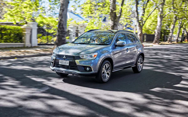 Silver Mitsubishi ASX SUV driving on a sunlit, tree-lined street — 2K Quad HD PC desktop wallpaper/background.
