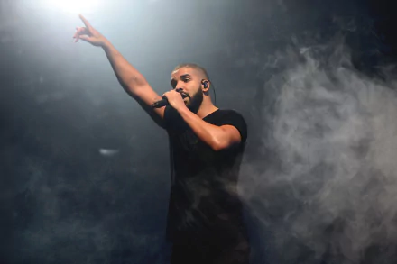 HD wallpaper of a performer on stage with a raised finger, surrounded by atmospheric stage smoke, creating an energized backdrop.