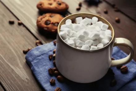 A 4K Ultra HD wallpaper featuring a white mug filled with mini marshmallows on a blue cloth, surrounded by coffee beans and chocolate chip cookies on a wooden table.
