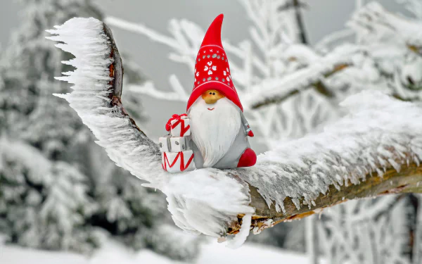 HD desktop wallpaper featuring a festive gnome ornament with a red hat and a gift, perched on a snow-covered, icy branch, set against a wintry forest background. Holiday and Christmas theme.
